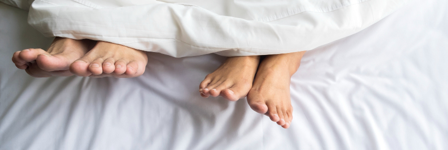 pareja en la cama, asomando los pies debajo de las sábanas después de hacer el amor